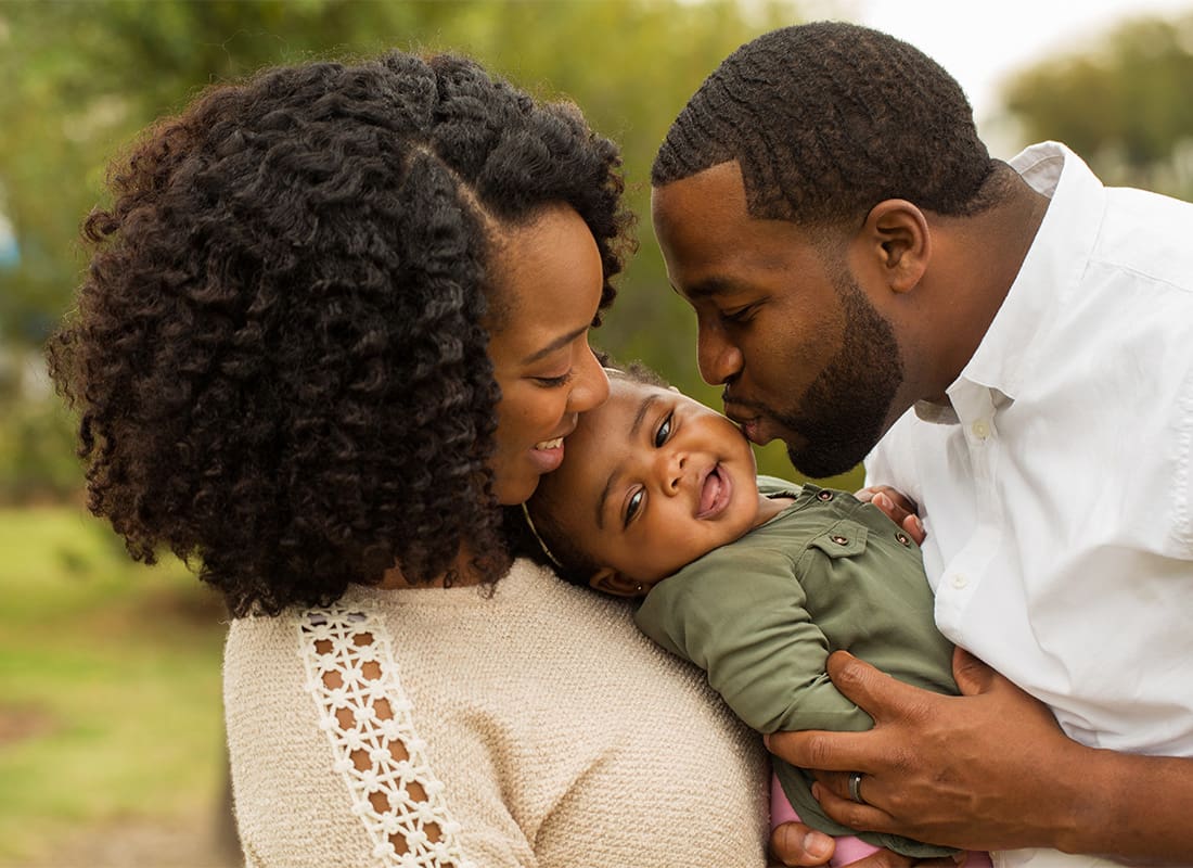 Personal Insurance - Young Married Couple Holding Their Daughter While Smiling