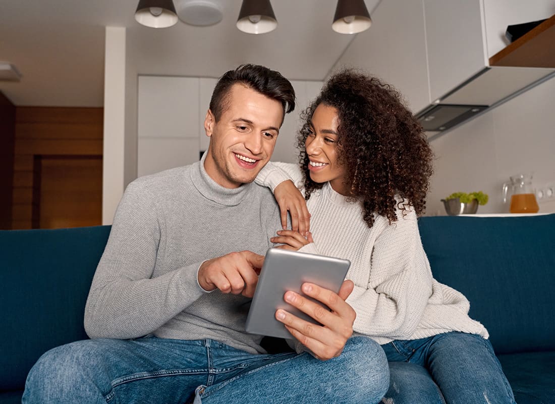 We Are Independent - Portrait of a Cheerful Young Married Couple Sitting on the Sofa in the Living Room While Using a Tablet